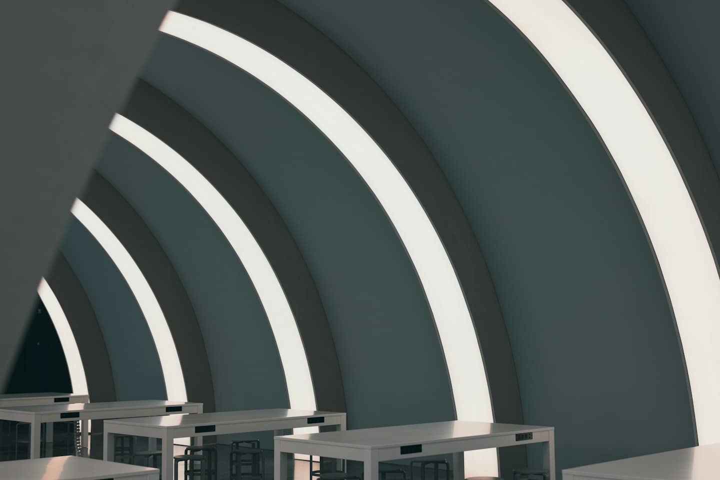 Home Pareti curve con illuminazione a strisce e tavoli bianchi in uno spazio di coworking moderno.